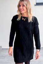 Robe pull courte noire en maille torsadée, des collants noirs et des bottines.