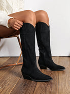 Bottes santiags noires effet daim (suédine), coupe mi-mollet, portées avec une robe pull en maille écru.