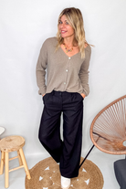 Gilet cardigan taupe maille fine porté rentré dans un pantalon large noir, look chic et confortable.