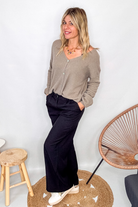 Gilet cardigan taupe maille fine porté rentré dans un pantalon large noir, look chic et confortable.
