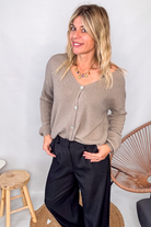 Gilet cardigan taupe maille fine porté rentré dans un pantalon large noir, look chic et confortable.