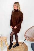Robe pull marron chocolat col roulé avec poches, coupe ample, portée avec des collants noirs et des bottines.