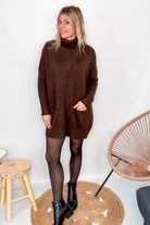 Robe pull marron chocolat col roulé avec poches, coupe ample, portée avec des collants noirs et des bottines.