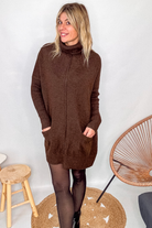 Robe pull marron chocolat col roulé avec poches, coupe ample, portée avec des collants noirs et des bottines.