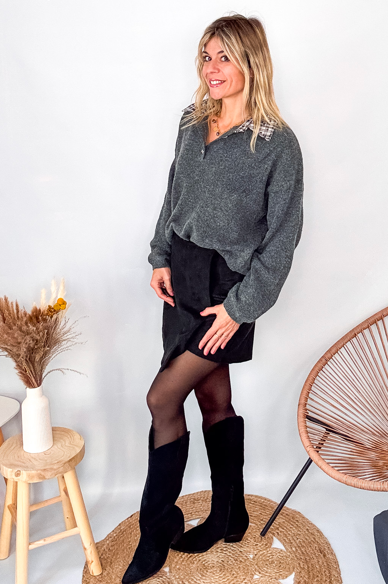 Pull gris chiné avec col en tissu imprimé carreaux, porté rentré dans une jupe noire suédine avec des collants opaques et des bottes.