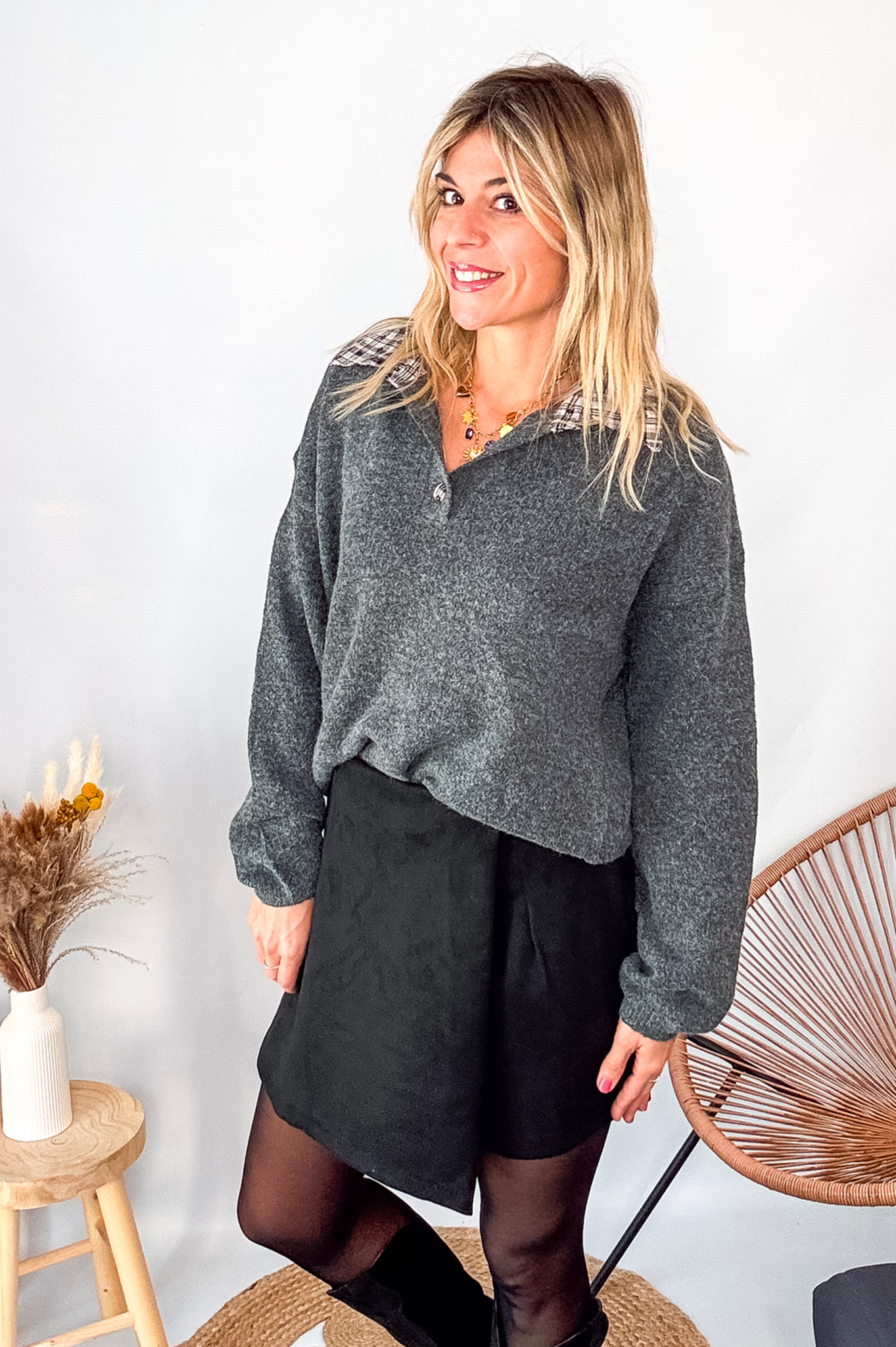 Pull gris chiné avec col en tissu imprimé carreaux, porté rentré dans une jupe noire suédine avec des collants opaques et des bottes.