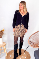 Gilet cardigan noir Baby Alpaga col V, porté sur une jupe courte imprimée léopard et des bottes noires hautes.