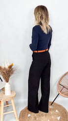 Pantalon tailleur noir fluide, coupe droite, porté avec un pull bordeaux et des accessoires.
