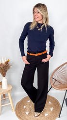 Pantalon tailleur noir fluide, coupe droite, porté avec un pull bordeaux et des accessoires.