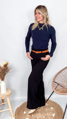 Pantalon tailleur noir fluide, coupe droite, porté avec un pull bordeaux et des accessoires.