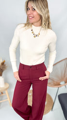 Pull fin beige col rond en maille douce, coupe droite, porté rentré dans un pantalon foncé.