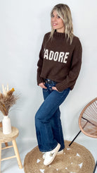 Pull marron col roulé maille, fabriqué en Italie, porté rentré dans un pantalon foncé.