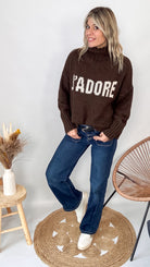 Pull marron col roulé maille, fabriqué en Italie, porté rentré dans un pantalon foncé.