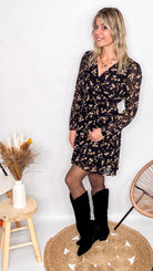 Robe noire fleurie 100% polyester, coupe fluide, portée avec des collants et des bottines.