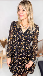 Robe noire fleurie 100% polyester, coupe fluide, portée avec des collants et des bottines.