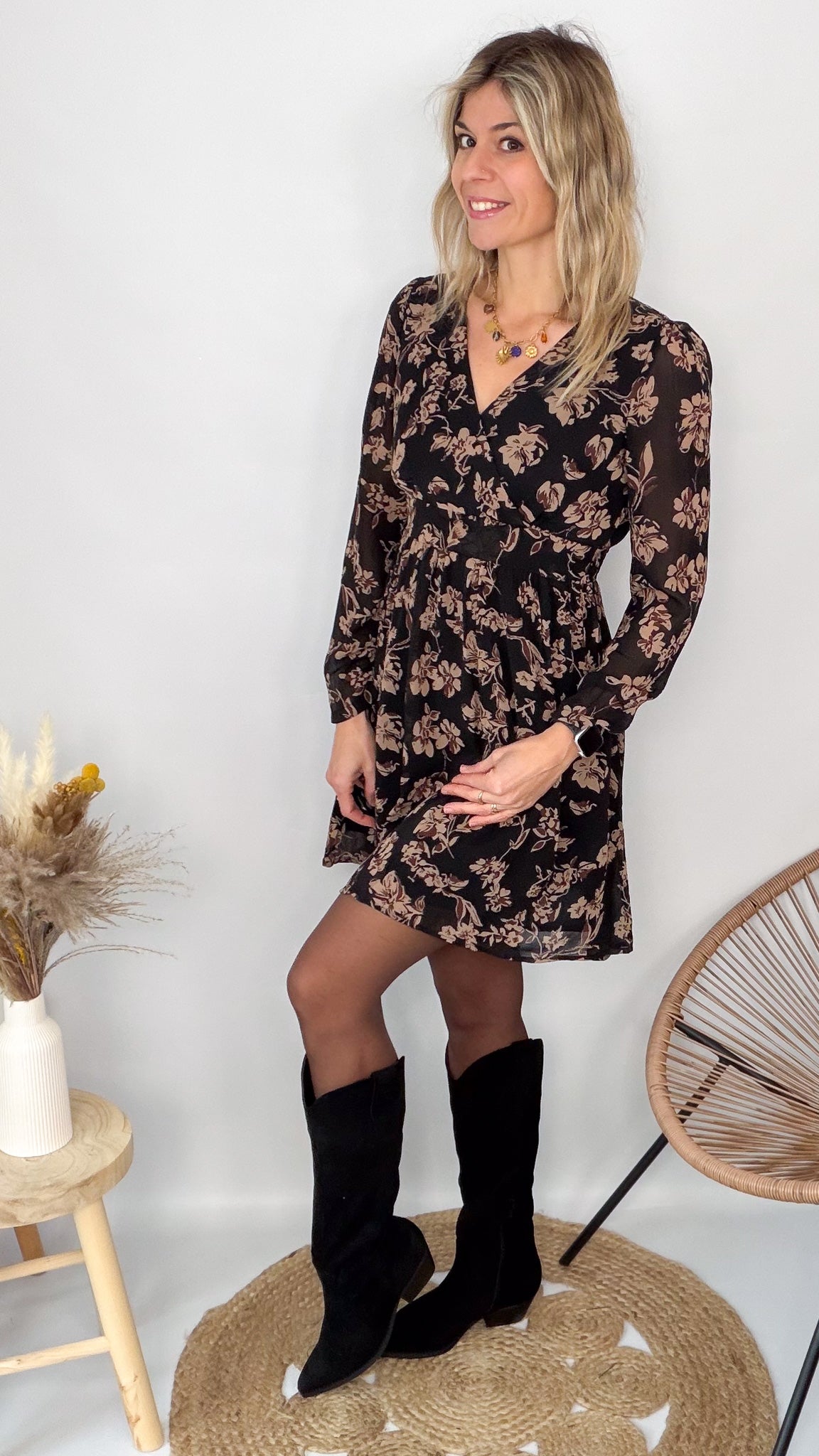Femme portant une robe noire courte à fleurs avec des bottes noires - Prêt-à-porter La Boutique de Lydie.